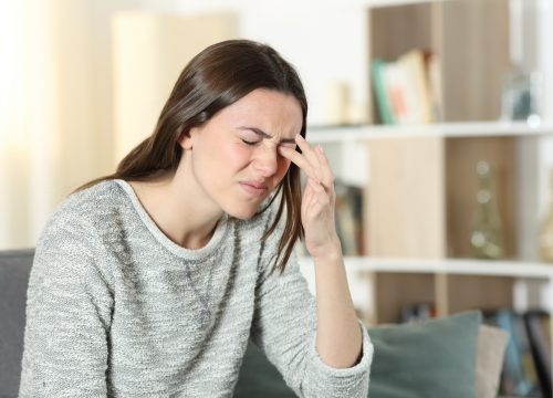 Woman scratching itchy eye at home.