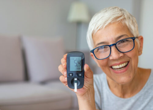 Photo of a happy older woman wearing glasses, checking her blood sugar