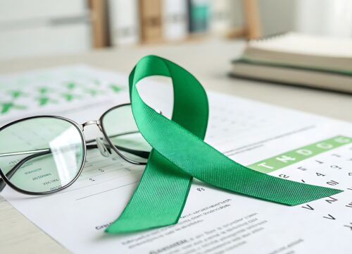 Photo of a green ribbon representing National Glaucoma Awareness Month next to eye glasses and an eye chart