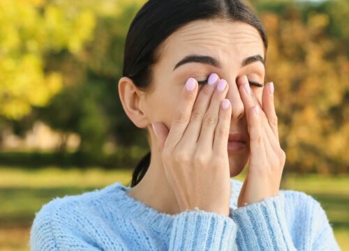 Photo of a woman experiencing dry eyes and allergies outside on a spring day